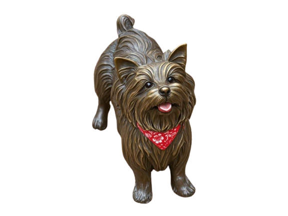 A bronze sculpture of a Yorkshire Terrier wearing a red bandana. The dog is sitting and looking at the viewer.